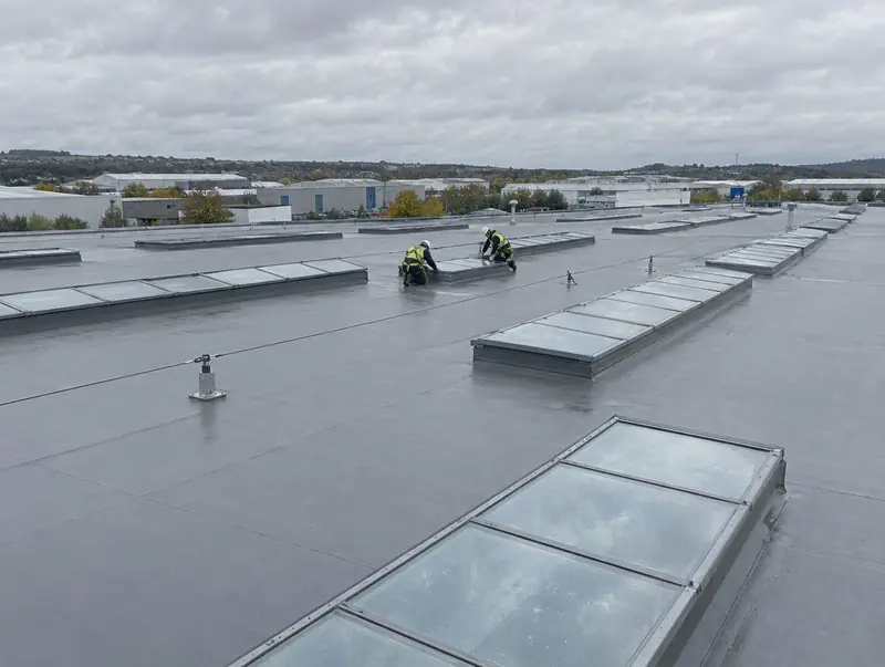 Fitters in harnesses working on rows of rooflights across a warehouse roof